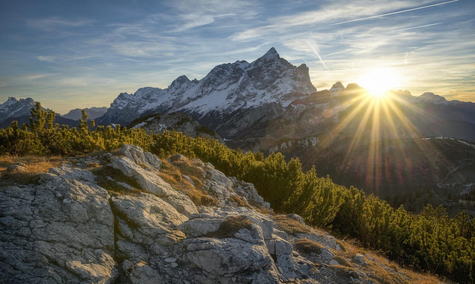 Stunning sunrise casting rays over the Italian Alps in Alleghe, Veneto, with lush greenery and rocky terrain.