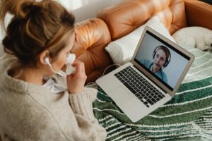 Woman having an online medical consultation on a laptop from her cozy sofa.