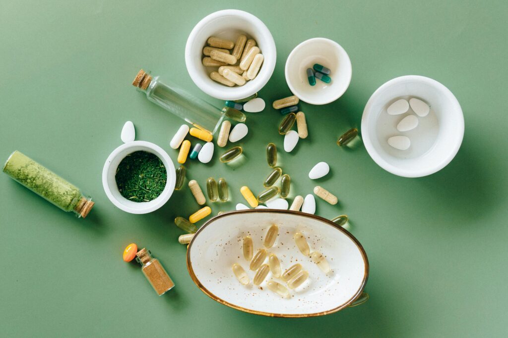 Top view of various herbal and pharmaceutical supplements in ceramic bowls on a green background.