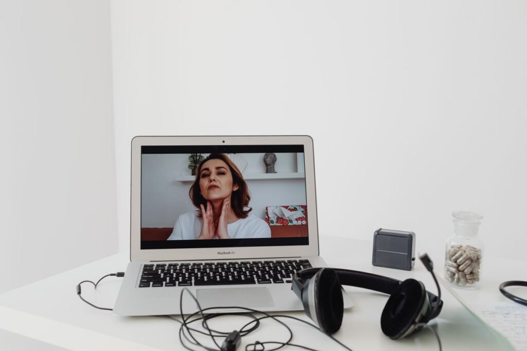 A woman conducting a telemedicine session visible on a laptop screen with headphones nearby.